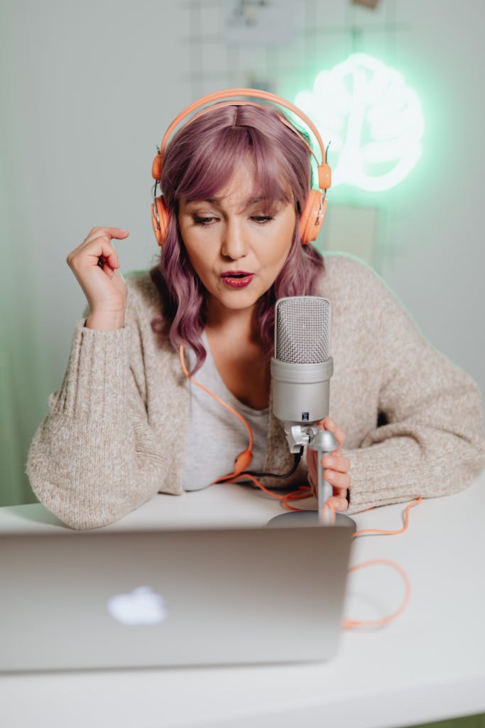 A woman wearing headphones, podcasting with a professional microphone and laptop.